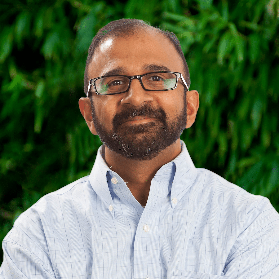 A strategic man with glasses and a beard standing in front of a tree.