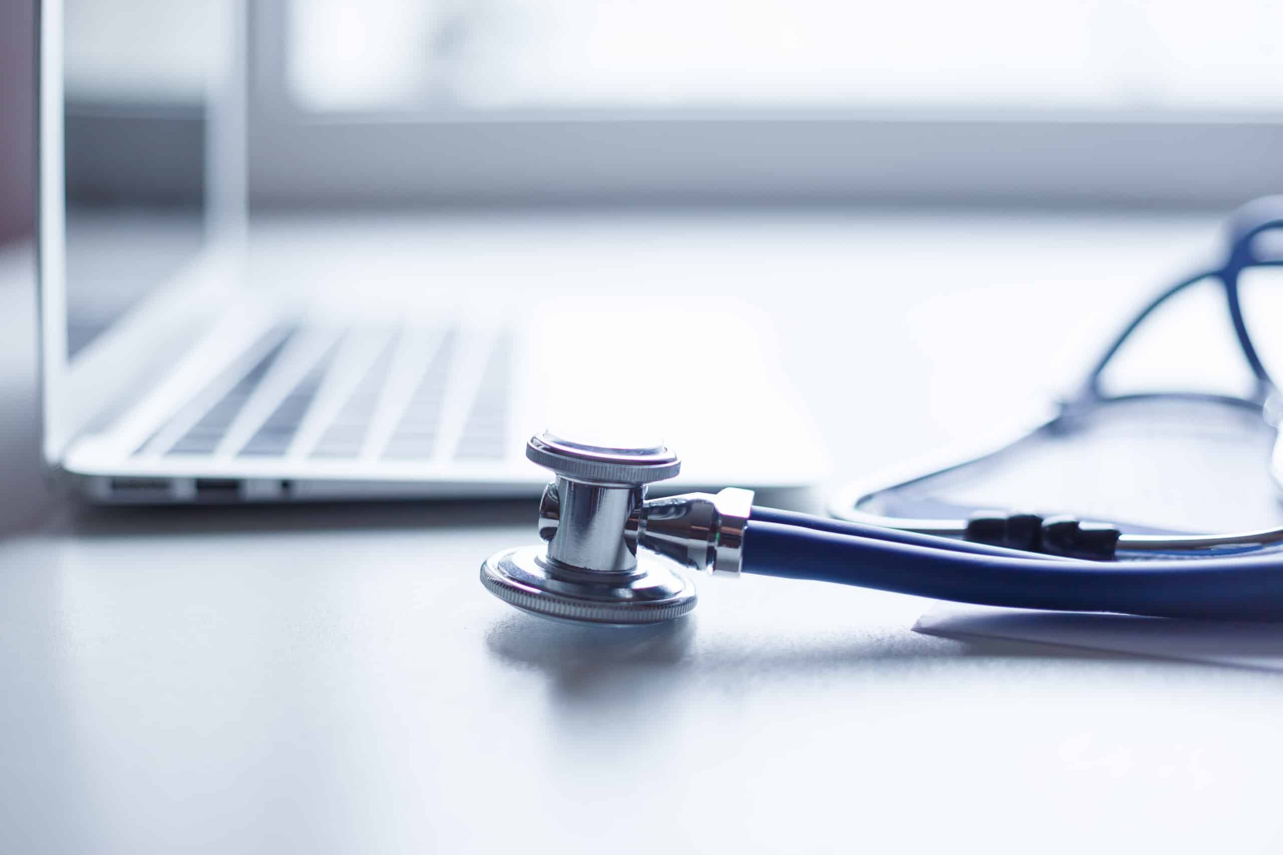 A stethoscope on a desk next to a laptop in a strategic company.