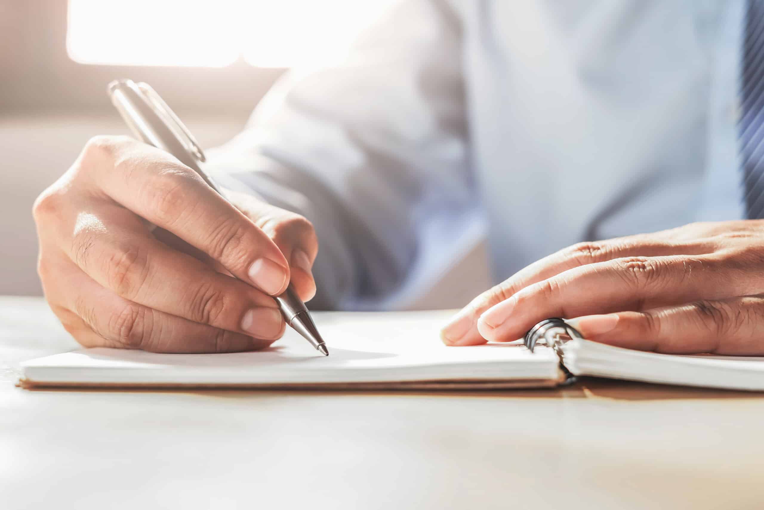 A man strategically consulting while writing in a notebook with a pen.