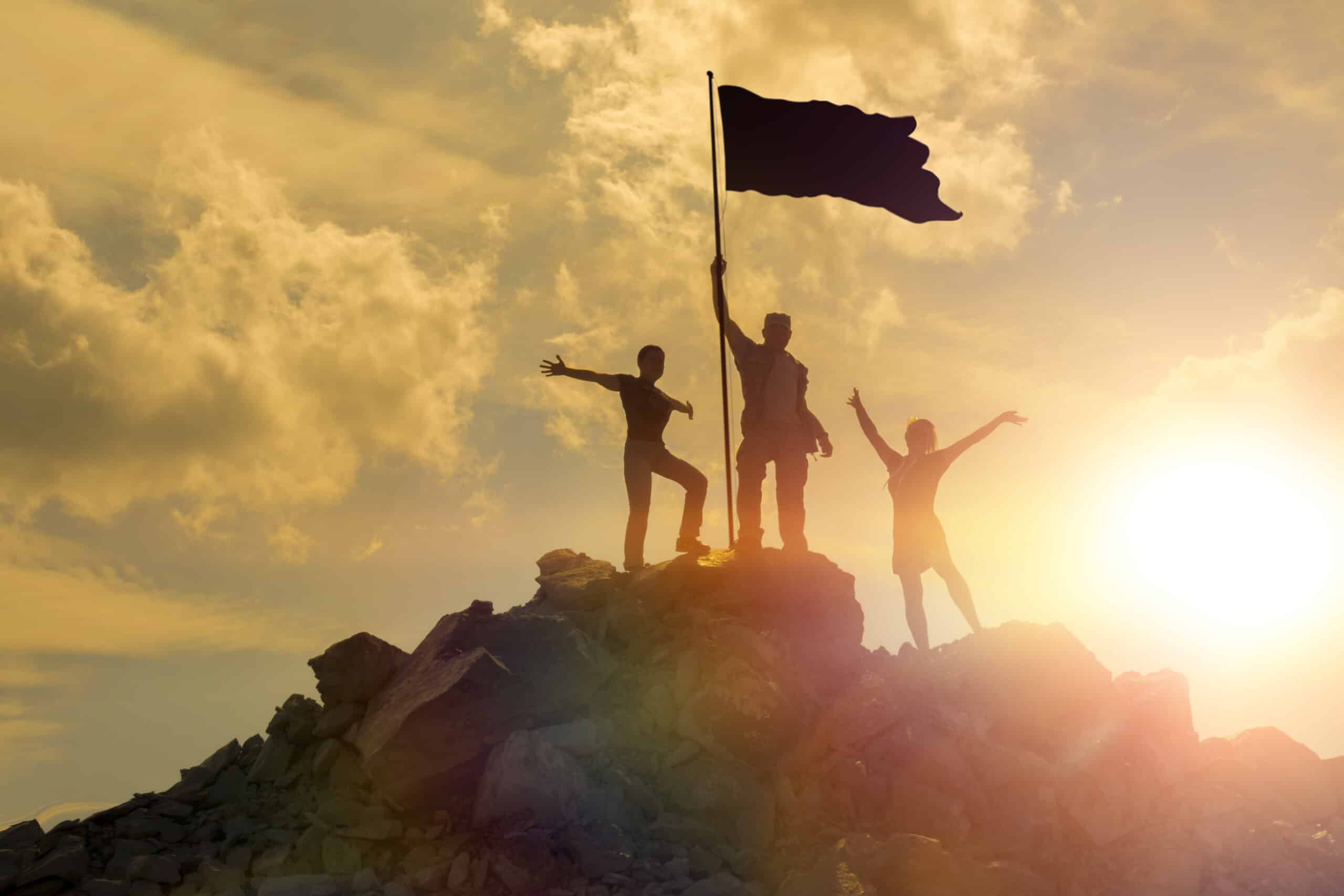 Three people standing on top of a mountain with an innovation flag.