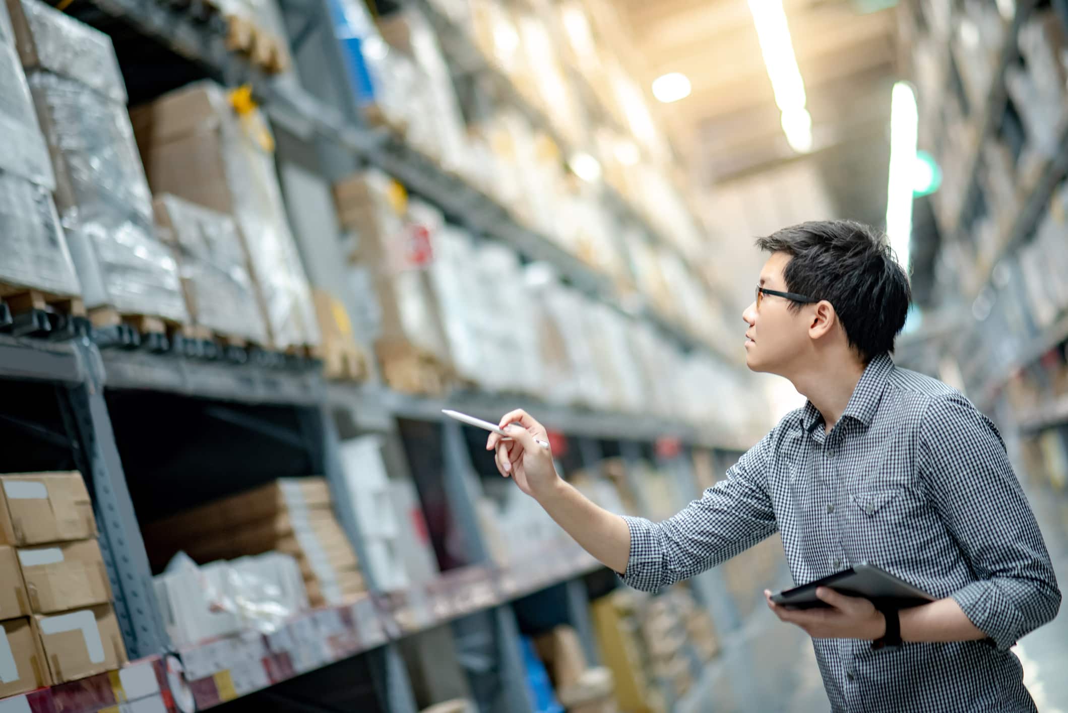 A strategic consultant in a warehouse holding a tablet.