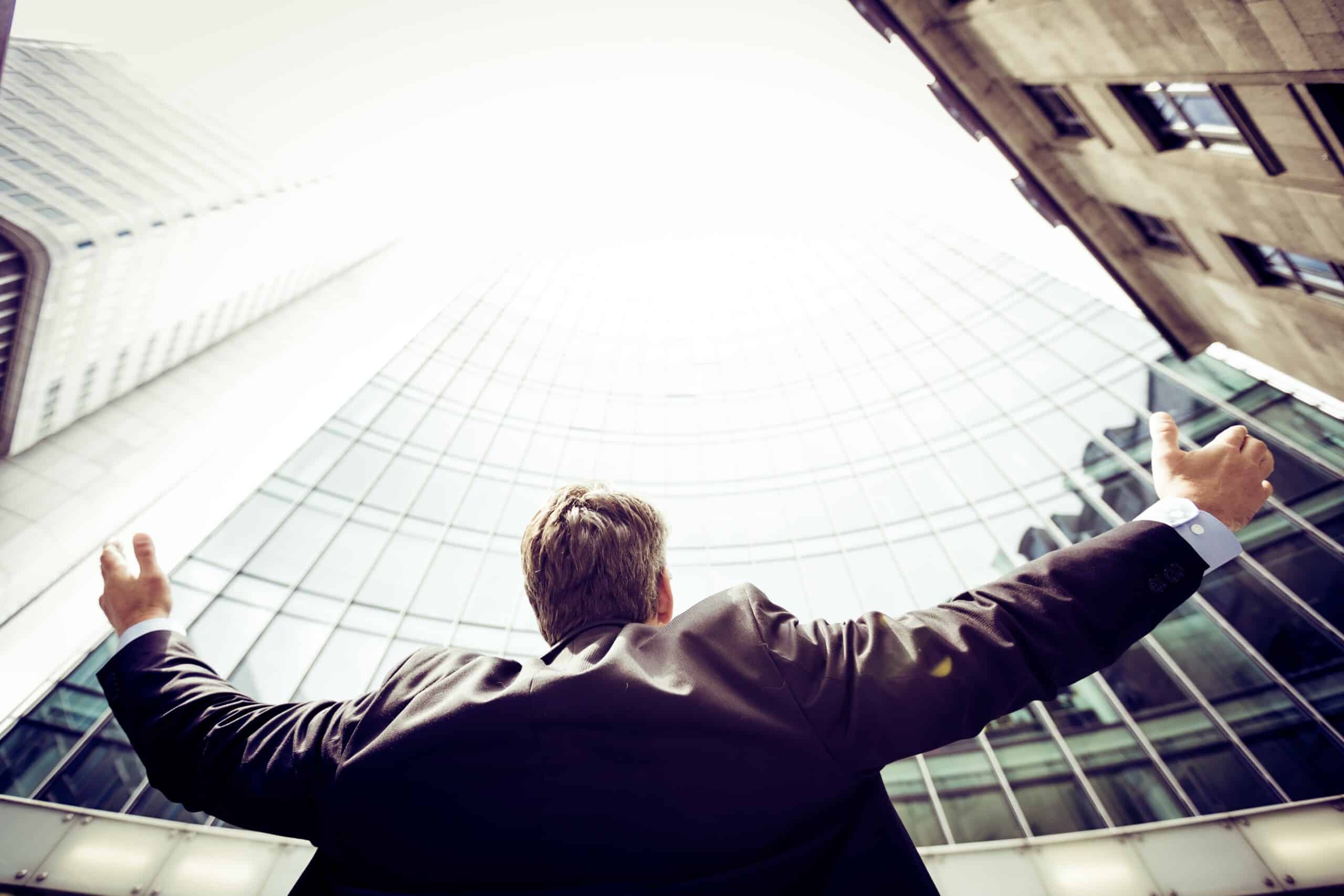 A tech businessman with his arms outstretched in front of a global company skyscraper.