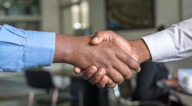Two strategic business people shaking hands in a tech company office.