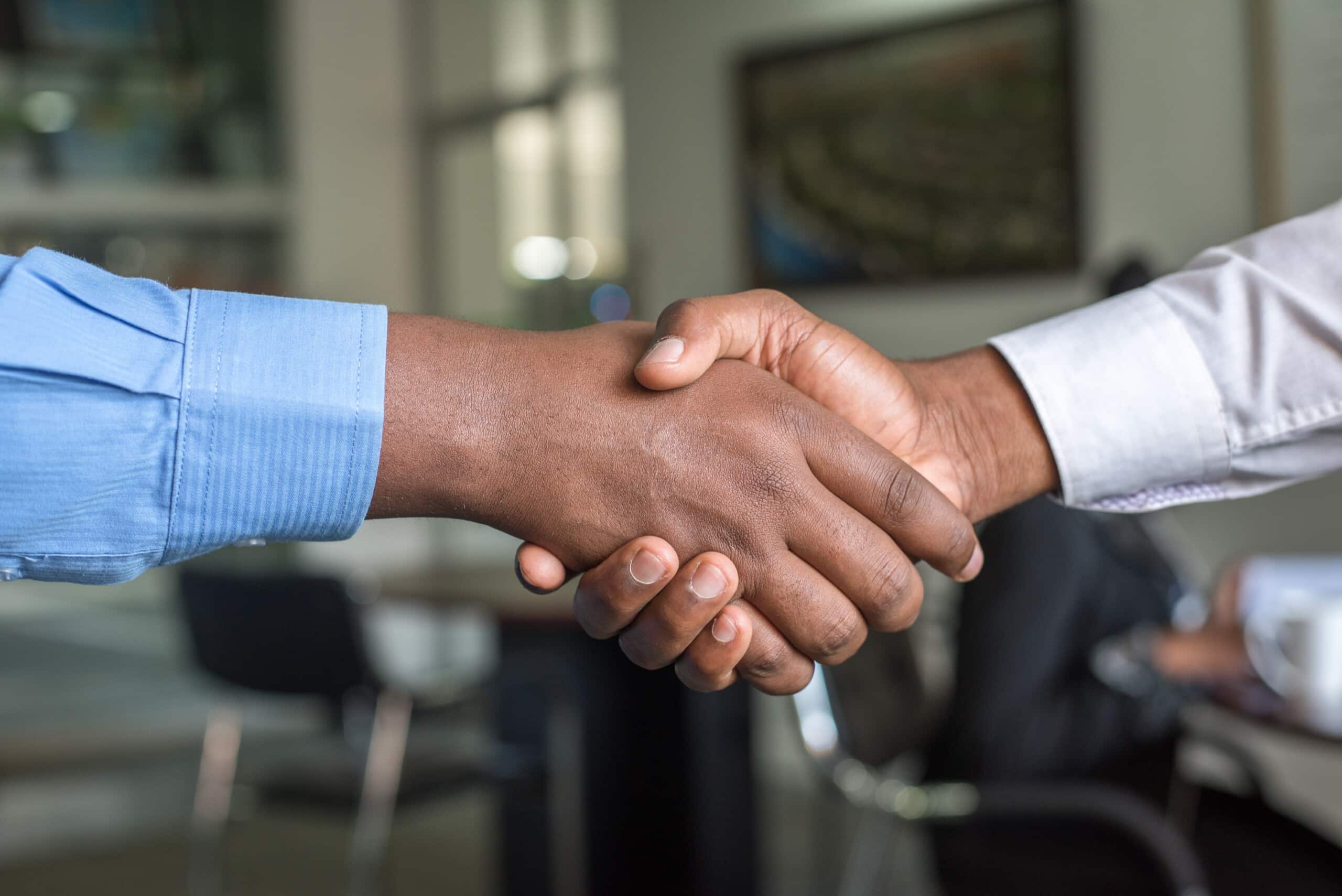 Two strategic business people shaking hands in a tech company office.