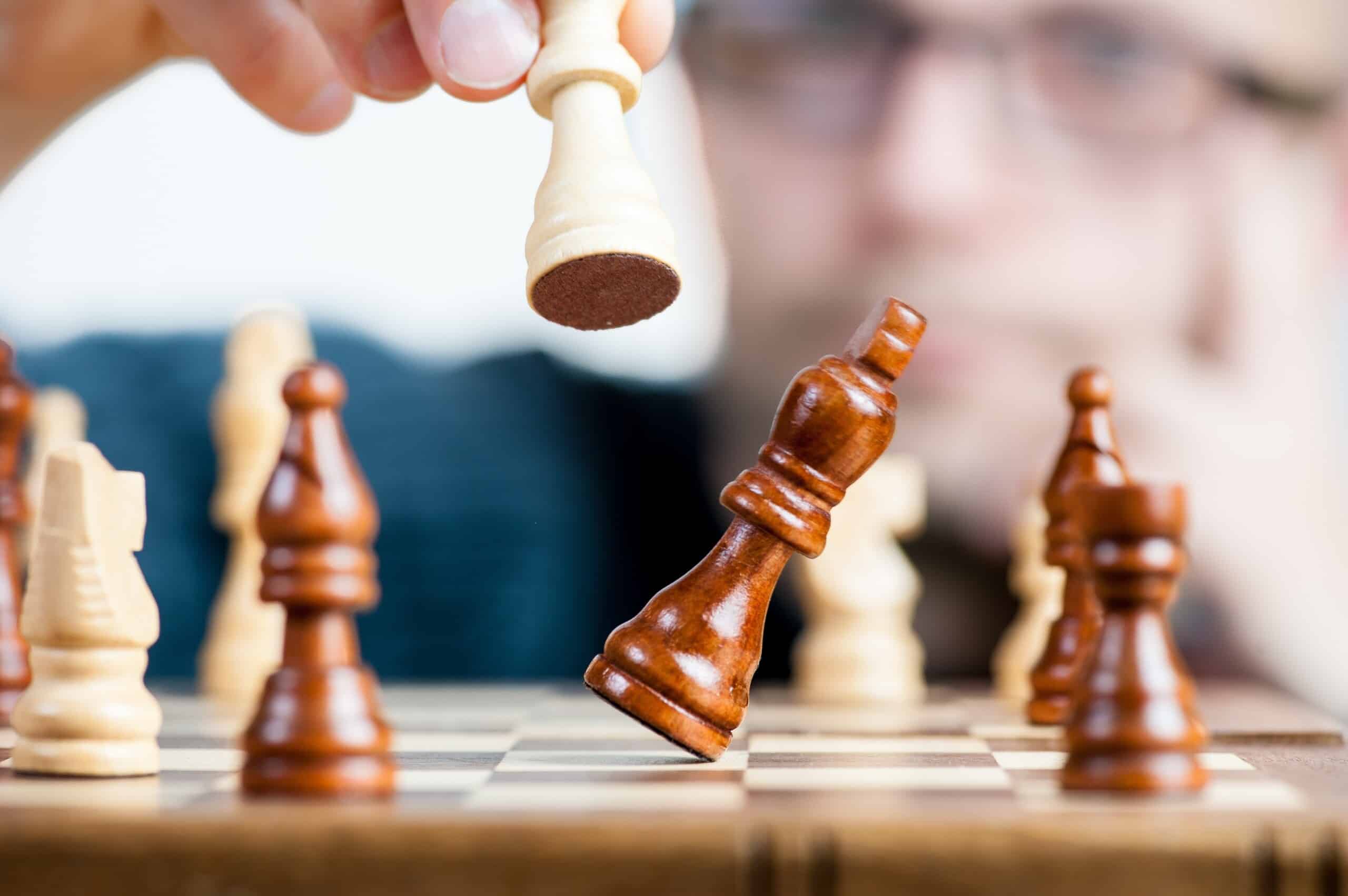 A strategic man is playing chess on a wooden board.