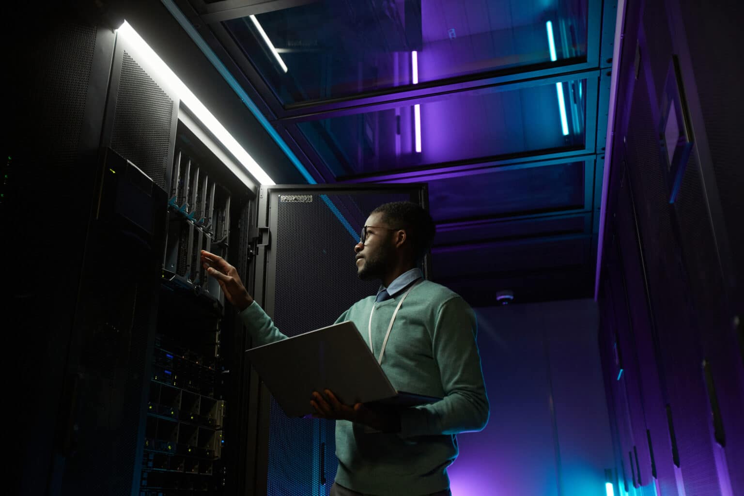 A global man in a server room looking at his laptop.