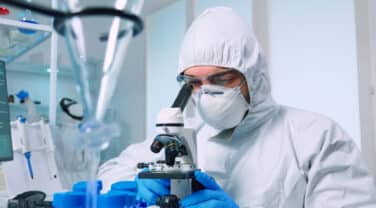 A strategic man in a lab coat is innovatively looking through a microscope.