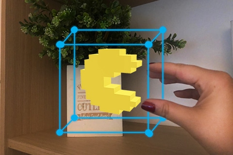 A tech-savvy individual strategically holds a yellow Pacman toy in front of a vase.
