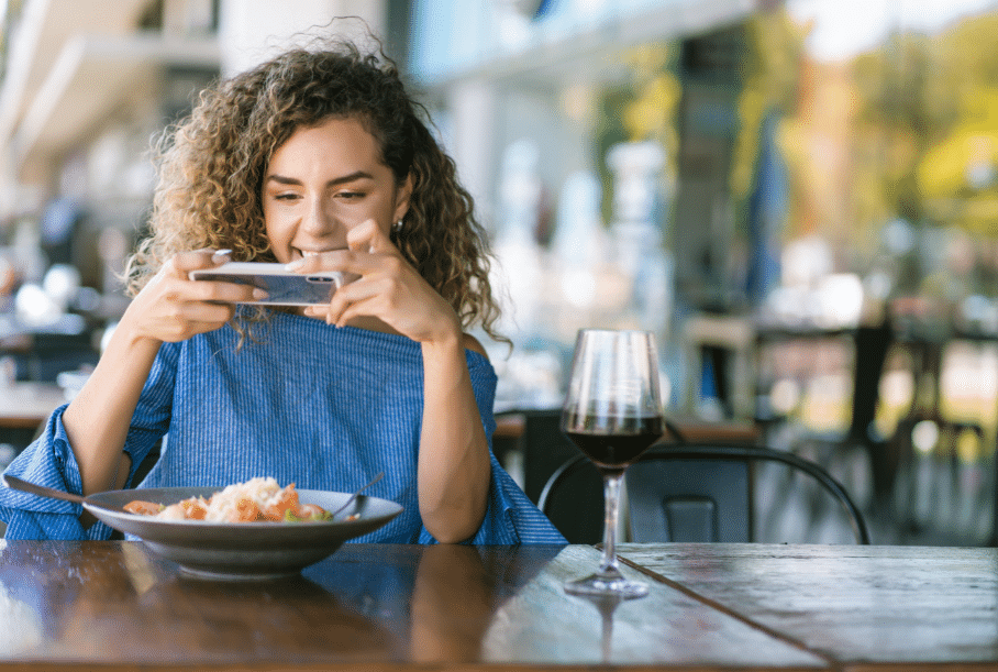 A woman strategically capturing her delicious food with the help of modern technology at a table.