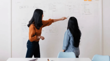 Two women pointing at a whiteboard in a tech office.