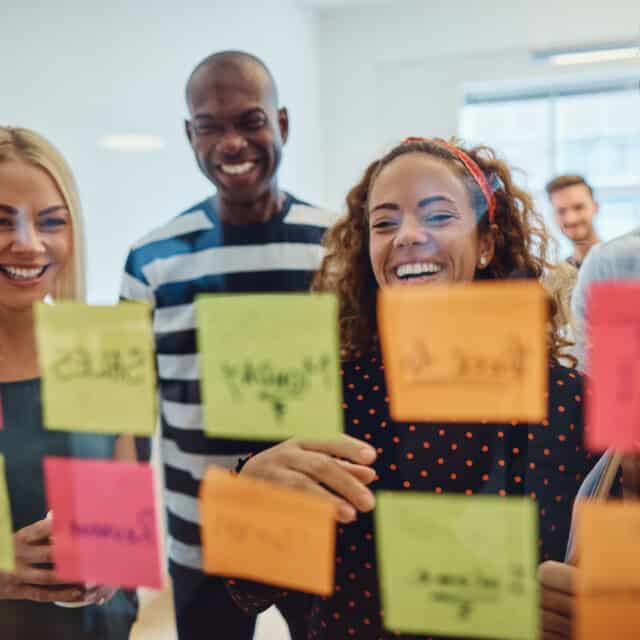 A global consulting company with a group of people standing around a board with sticky notes on it.