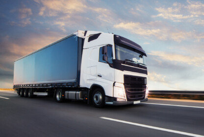 A semi truck driving on a highway at sunset.